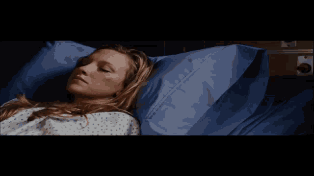 a woman laying in a hospital bed with a blue pillow