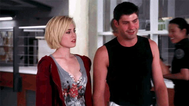 a man in a black tank top stands next to a blonde woman