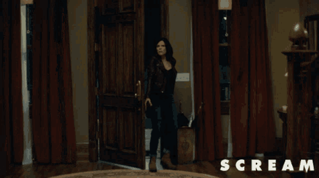 a woman is standing in a room with the word scream on the bottom right