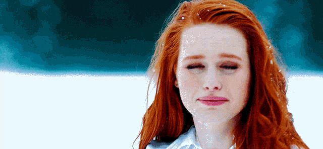 a woman with red hair is standing in the snow making a funny face .