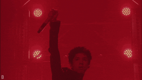a man holding a microphone in front of a red background with the letter d on the bottom