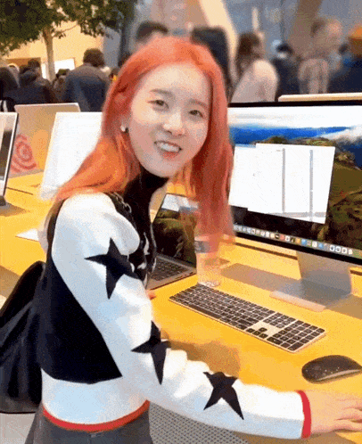 a woman with red hair is sitting at a desk with a mac computer