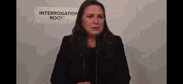 a woman in a black suit is standing in front of a sign that says interrogation room .