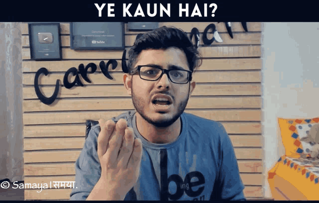 a man wearing glasses and a blue shirt that says be