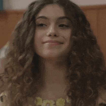 a woman with long curly hair is smiling and making a funny face .