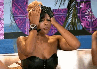 a woman in a black strapless top is covering her face with her hands while sitting on a couch .