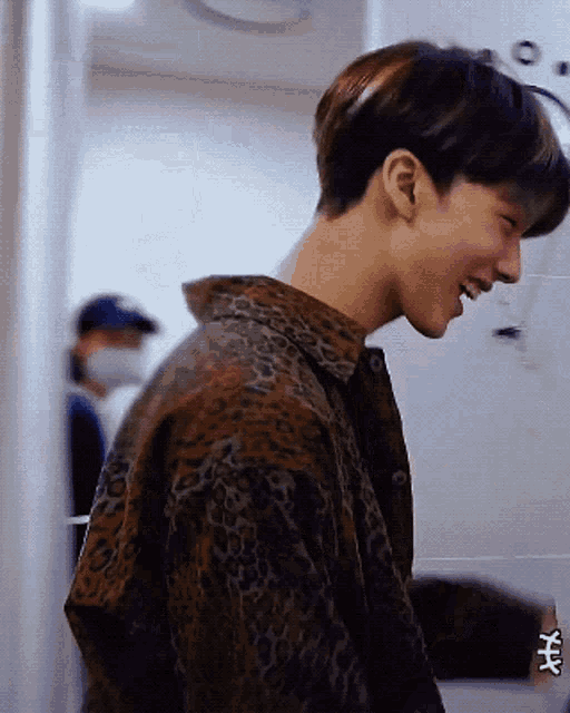 a young man wearing a leopard print shirt is smiling and looking over his shoulder