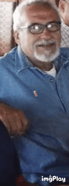 a man wearing glasses and a blue shirt is smiling