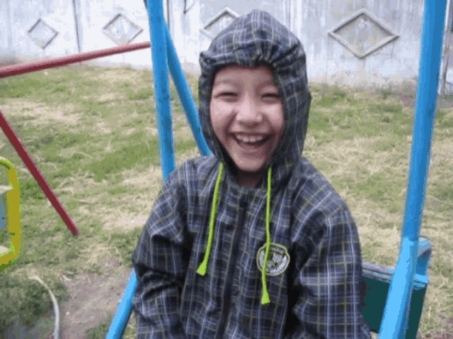 a young boy wearing a plaid jacket with a hood smiles