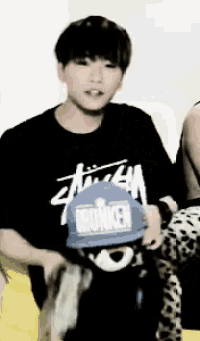 a man wearing a black stussy shirt is holding a blue hat that says wunken