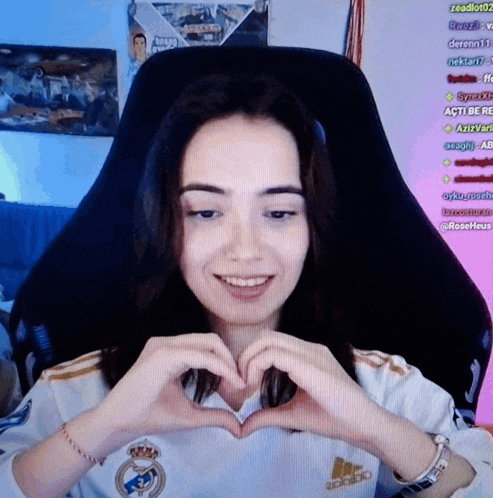 a woman making a heart shape with her hands while wearing a real madrid jersey