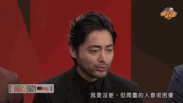 a man in a black suit is talking to someone in a foreign language