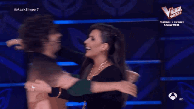 a man and a woman are dancing in front of a sign that says la voz