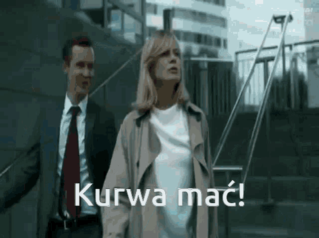 a man in a suit and tie is walking next to a woman in a trench coat and stairs .