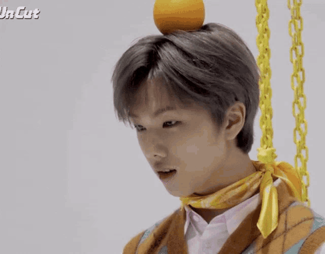 a young man with an orange on his head is wearing a yellow scarf around his neck