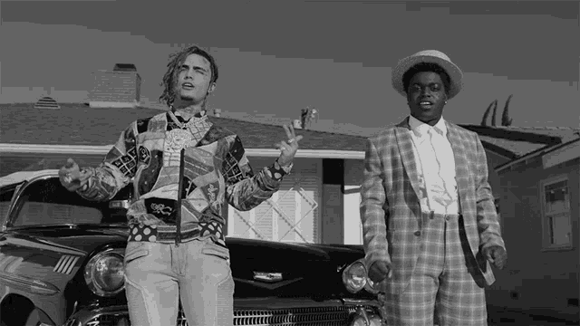 a man in a plaid suit stands next to a man in a hat
