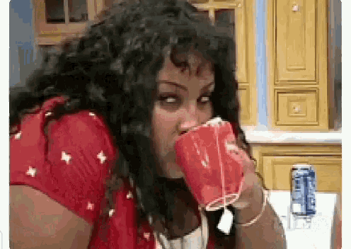 a woman in a red shirt is drinking from a plastic cup