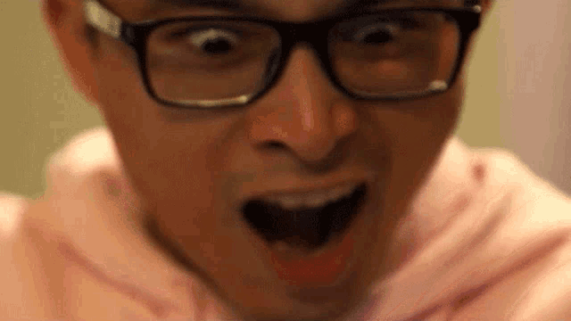 a man wearing glasses and a pink hoodie is making a surprised face .
