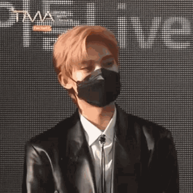 a young man wearing a black mask and a leather jacket is standing in front of a microphone .