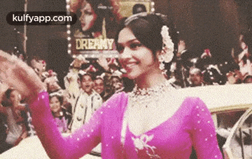 a woman in a pink blouse is waving at a crowd of people .