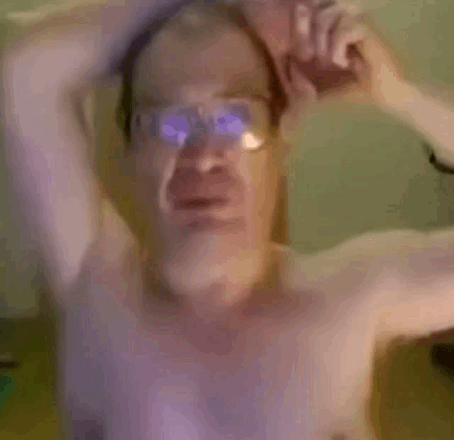 a shirtless man wearing glasses is making a funny face while holding his head .
