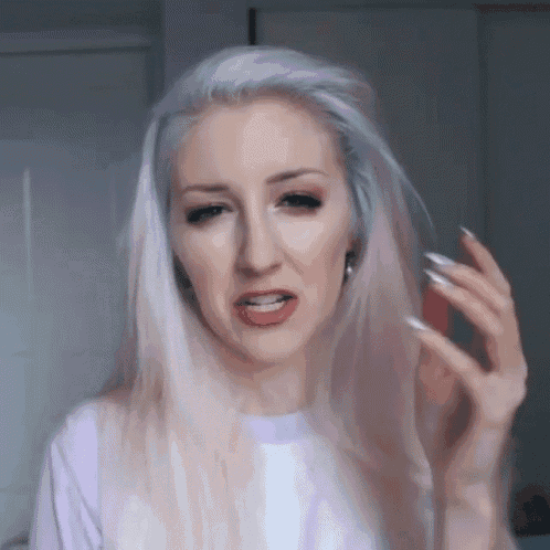 a woman with long white hair is wearing a purple shirt and making a funny face .