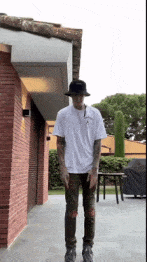 a man wearing a white t-shirt and a black hat is standing in front of a brick building