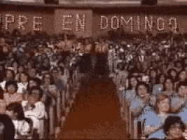 a man stands in front of a crowd with siempre en domingo written on the wall behind him