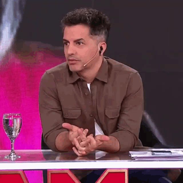 a man wearing a microphone is sitting at a table with a glass of water .