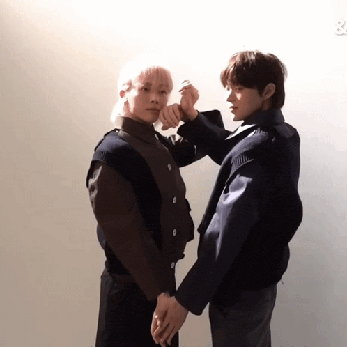 two young men are holding hands while standing next to each other against a white wall