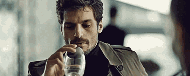 a man in a trench coat is drinking water from a glass