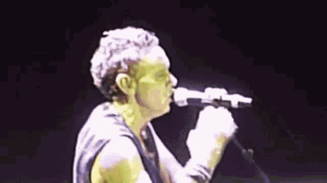 a man is singing into a microphone on a stage in a dark room .