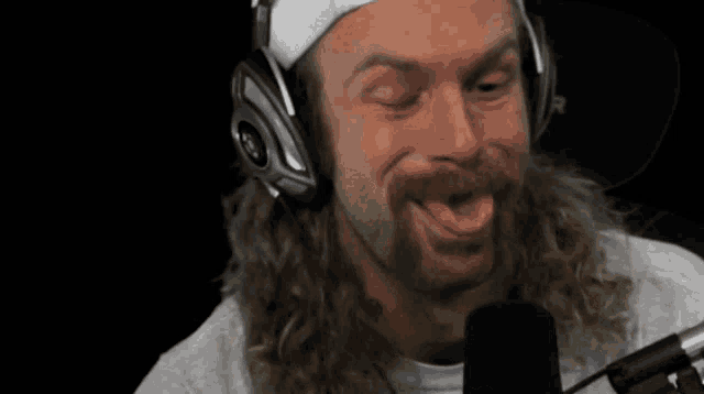 a man with a beard wearing headphones and a headband is sticking his tongue out