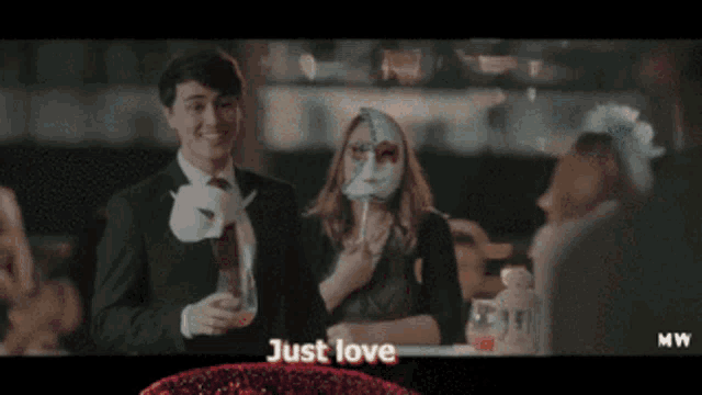 a man in a suit stands next to a woman wearing a mask that says just love on it