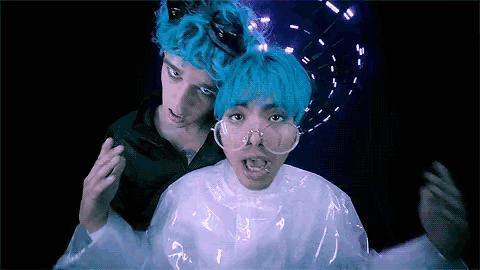 a man with blue hair and glasses stands next to another man with blue hair