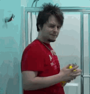 a man in a red shirt is standing in a bathroom holding a bottle of lotion .