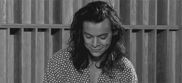 harry styles is smiling in a black and white photo in front of a wooden fence .