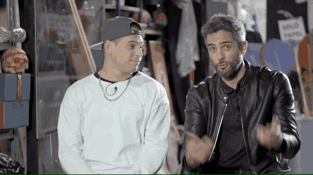 two men sitting next to each other one wearing a white sweatshirt that says city of kings