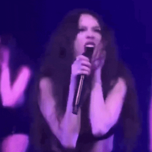 a woman is singing into a microphone on stage in front of a purple background .