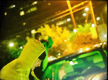 a person wearing a yellow hoodie is standing in front of a green car