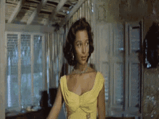 a woman in a yellow dress is standing in a room and looking at the camera .