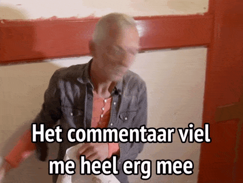 a man standing in front of a red door with the words het commentaar viel me heel erg mee written on it