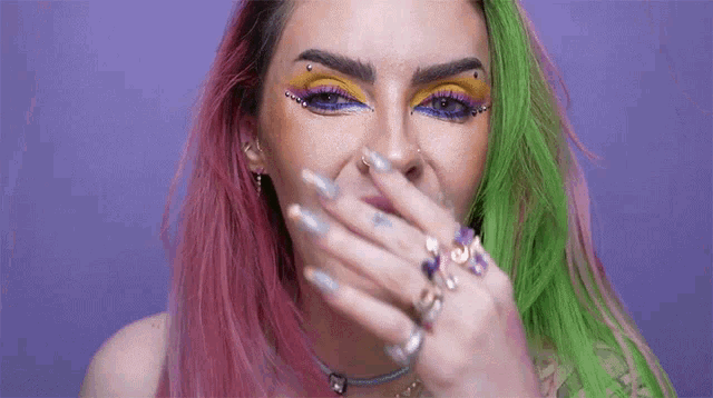 a woman with pink and green hair is covering her mouth with her hand