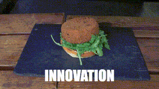 a hamburger with lettuce on a bun is on a slate plate with the word innovation below it