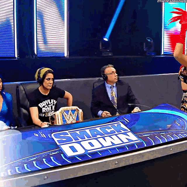 a woman in a boyley role shirt sits in front of a table that says smack down