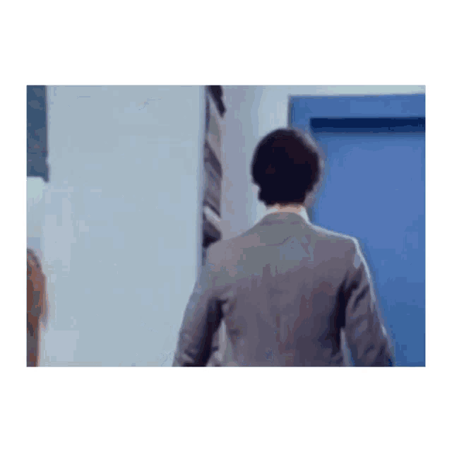 a man in a suit and tie is walking through a blue door .