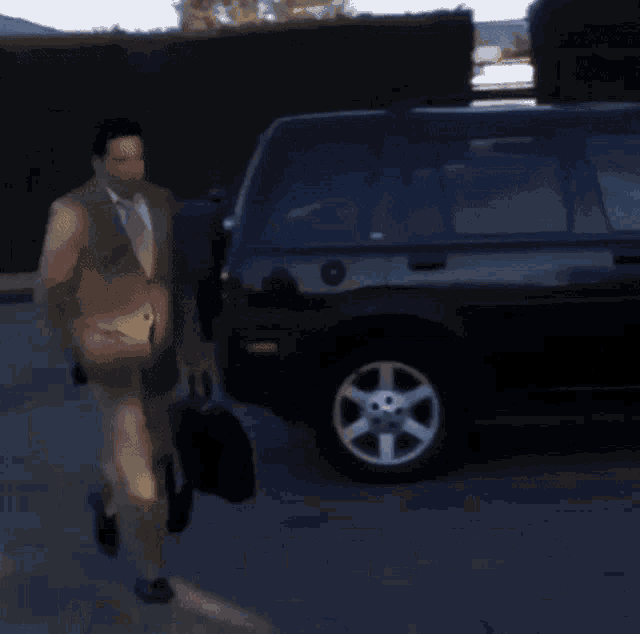 a man in a suit and tie is walking towards a black car