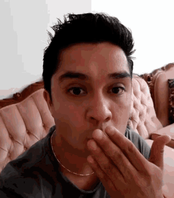 a man is covering his mouth with his hands and looking at the camera .