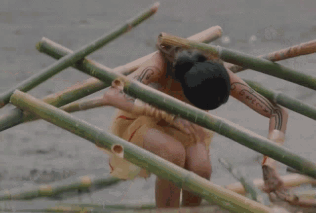 a person with a tattoo on their arm is laying on a pile of bamboo sticks
