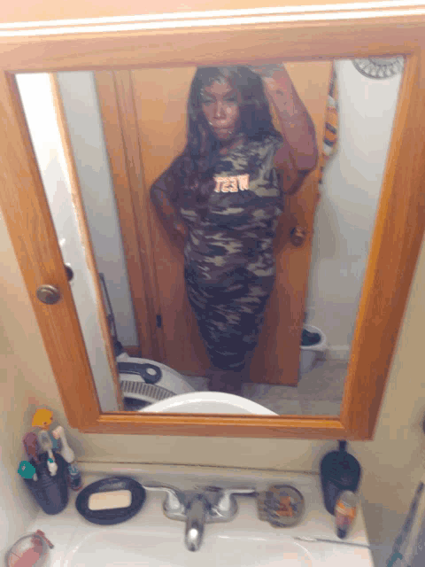 a woman taking a picture of herself in a bathroom mirror with the word jesus on her shirt